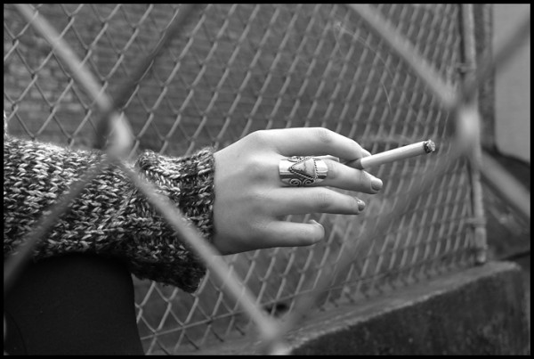 I liked the elegance of her hand, the ring and sweater juxtaposed with the cigarette framed by the chain link fence.